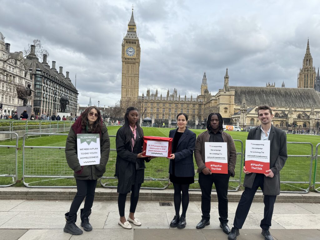 Nadia Whittome MP stands in the middle holding the box, with young people around her. In the background is the Houses of Parliament, Big Ben against a grey sky.