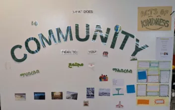 A white wall with big green letters spelling Community. Around are post it notes and words all about community