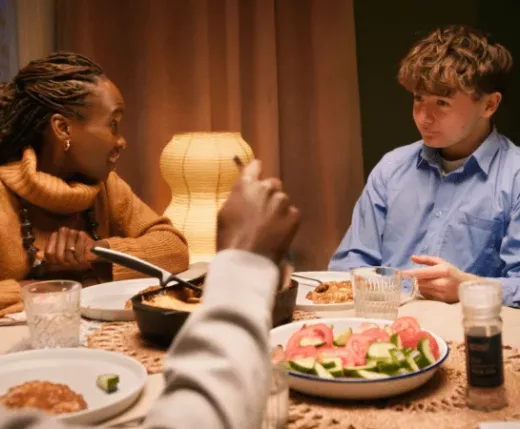 A family eating dinner at a table. A woman is talking to a young man