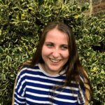 Photo of Martha, a white woman with long brown hair wearing a blue and white striped top