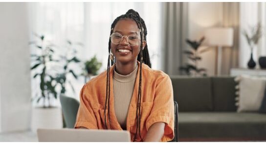 Black woman, portrait in home office and laptop for remote work, social media or blog research with smile in apartment. Happy freelancer at desk with computer for email, website or online in house